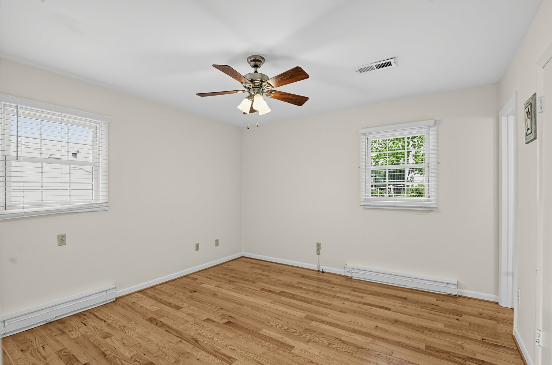 Bright bedroom with hardwood floors, two windows and a ceiling fan